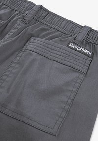 Dark gray pants with an elastic waistband, back pocket with double stitching, and a black patch labeled "Abercrombie" near the pocket.