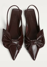 Dark brown pointed slingback shoes with large bow detail on top, displayed side by side on a white background.