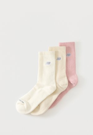 Tre ribstrikkede crew-sokker i creme, beige og pink, hver med et lille gråt logo på ankelområdet, arrangeret overlappende på en hvid baggrund.