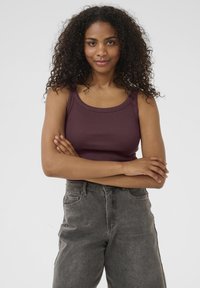 Débardeur côtelé bordeaux à encolure large, associé à un jean en denim gris taille haute avec poches avant et coupe décontractée.