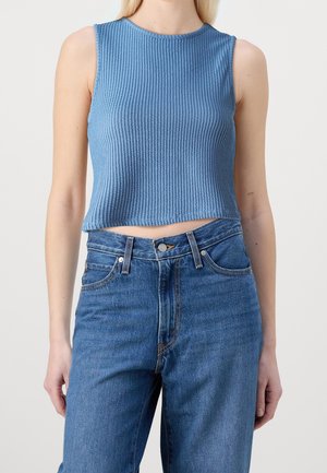 Niebieski bezrękawnik prążkowany crop top noszony z niebieskimi dżinsami z wysokim stanem na stojącej osobie.