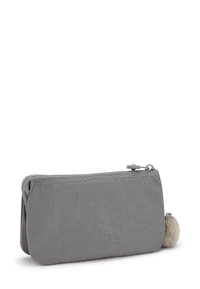Gray zippered pouch made of soft fabric, featuring a rounded shape and a fluffy pom-pom accent on one side.