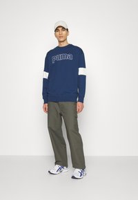 Navy blue sweatshirt with white stripes, featuring a prominent Puma logo. Paired with olive cargo pants and white sneakers.