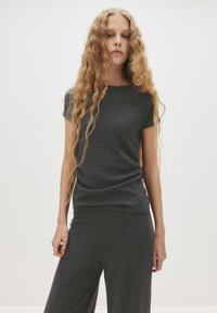 Tummanharmaa lyhythihainen t-paita, joka on valmistettu pehmeästä, teksturoidusta materiaalista. Tässä paidassa on pyöreä kaula-aukko ja slim fit -malli. Yhdistettynä matching tummiin housuihin.