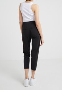 Pantaloni neri a sigaretta con vita elasticizzata, dotati di due tasche posteriori; modello abbinato a sneakers bianche. Tessuto liscio e design elegante.