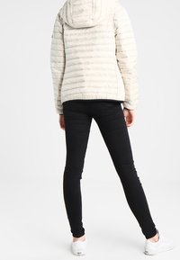 Světle barevná péřová bunda s horizontálním prošíváním, připevněná kapuce; v kombinaci s černými skinny džíny a bílými teniskami.