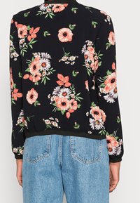 Bluza z kwiatowym wzorem, czarne tło, intensywne różowe i białe kwiaty, okrągły dekolt, ściągacze na rękawach i u dołu, luźne dopasowanie. W zestawieniu z niebieskimi dżinsami.