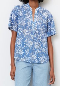 Blusa azzurro chiaro a maniche corte con un motivo floreale bianco, scollatura a V e vestibilità rilassata. Realizzata in un tessuto morbido con una texture liscia.