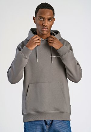 Gray hooded sweatshirt with a textured finish, featuring a front pocket, drawstrings, and small branding on the chest. Worn with blue jeans.