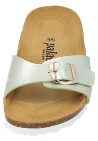 Ljusgrön lädersandalsko med slidkonstruktion som har ett guldspänne, mjukt mockainlägg och en brun texturerad korksula med en vit kant.