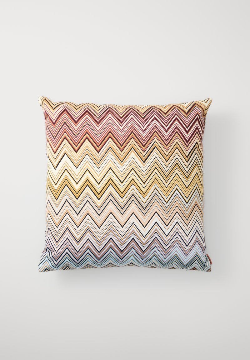 Firkantet dekorativ pute med et zigzag-mønster i rødt, gult, beige og blått. Laget av tekstil med en glatt tekstur og pipingkanter.