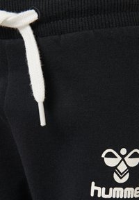 Pantalon de survêtement noir avec cordon blanc, doté d'une texture douce et d'un logo imprimé en blanc sur la jambe inférieure.