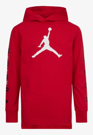 T-shirt à capuche rouge à manches longues avec une grande silhouette blanche d'un joueur de basket en train de sauter avec un ballon sur le devant et un texte noir sur les manches.