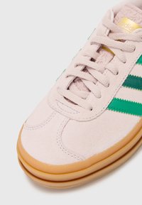 Ljusrosa mockaskor med gröna ränder, texturerad detaljering och gummisulor. Har snörningsdesign och logotyp på tungan.