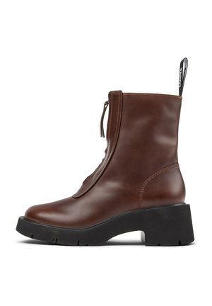 Brown leather ankle boot with black chunky sole, front zipper, and pull tab with white branding detail.