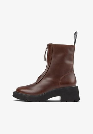 Braune Lederstiefelette mit schwarzem, klobigem Absatz, Reißverschluss vorne und einer Schlaufe mit weißem Branding-Detail.