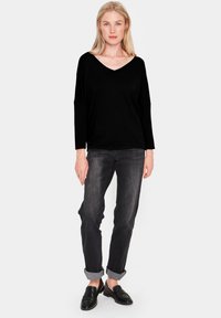 Svart V-ringad tröja med långa ärmar, kombinerad med mörka jeans, uppvikta ärmslut och svarta loafers. Slät textur genomgående.