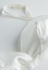 Soutien-gorge en satin blanc avec un tissu lisse, des bonnets doux et des bretelles étroites et réglables. Il dispose d'une fermeture à crochets et d'œillets et de détails de couture subtils.