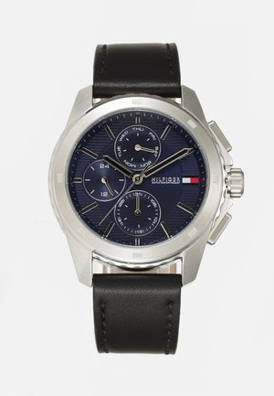 Reloj de metal plateado con un dial azul marino, tres sub-diales y una correa de cuero negra. Incluye indicador de fecha y acentos de bisel de acero.