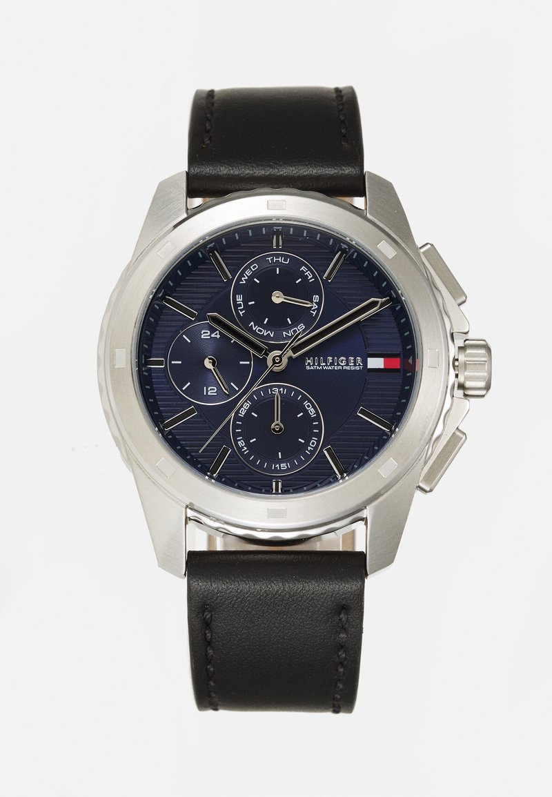 Reloj de metal plateado con un dial azul marino, tres sub-diales y una correa de cuero negra. Incluye indicador de fecha y acentos de bisel de acero.