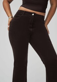 Schwarze samtige Schlaghosen aus Cord mit glatter Oberfläche, vorderen Taschen und Reißverschluss. Mit einem Metallknopf und einer Nahtdetail.