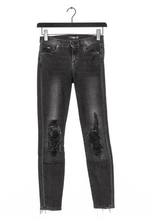 Schwarze, abgenutzte Skinny-Jeans mit zerrissenen Knien und ausgefransten Säumen, die an einem schwarzen Kleiderbügel vor weißem Hintergrund hängen.