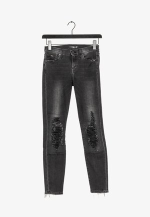 Zwarte distressed skinny jeans met gescheurde knieën en rafelige zoom, hangend aan een zwarte hanger tegen een witte achtergrond.