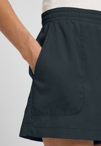 Dunkelgraue Sportshorts mit einem elastischen Bund und seitlichen Taschen, aus leichtem, glattem Material mit leichtem Glanz.