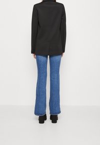 Svart skräddarsydd blazer med en enda bakslits, i kombination med ljusblå utsvängda jeans. Jeansen har en ren nederkant och minimala slitningar.