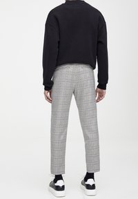 Czarna bluza, szare spodnie w kratę o slim fit i białe sneakersy z czarnymi akcentami. Widoczne szwy i długość do kostek.