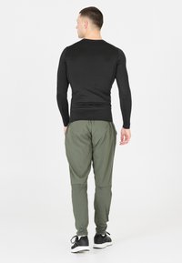 Zwart langemouwen shirt gecombineerd met olijfgroene joggers. Het shirt heeft een aansluitend ontwerp en de joggers hebben taps toelopende pijpen met elastische boorden.