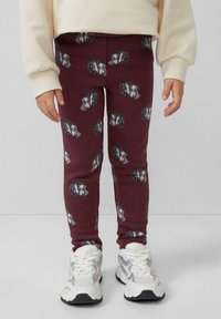 Burgundowe legginsy z szarym wzorem głowy zwierząt; miękki, elastyczny materiał; w połączeniu z białymi sneakersami z szarymi akcentami.