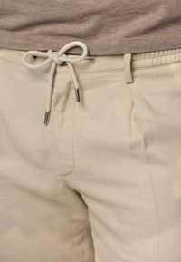 Beżowe lniane spodnie z regulowanym paskiem na sznurku, z metalowymi akcentami, bocznymi kieszeniami i miękkim, teksturowanym wykończeniem.