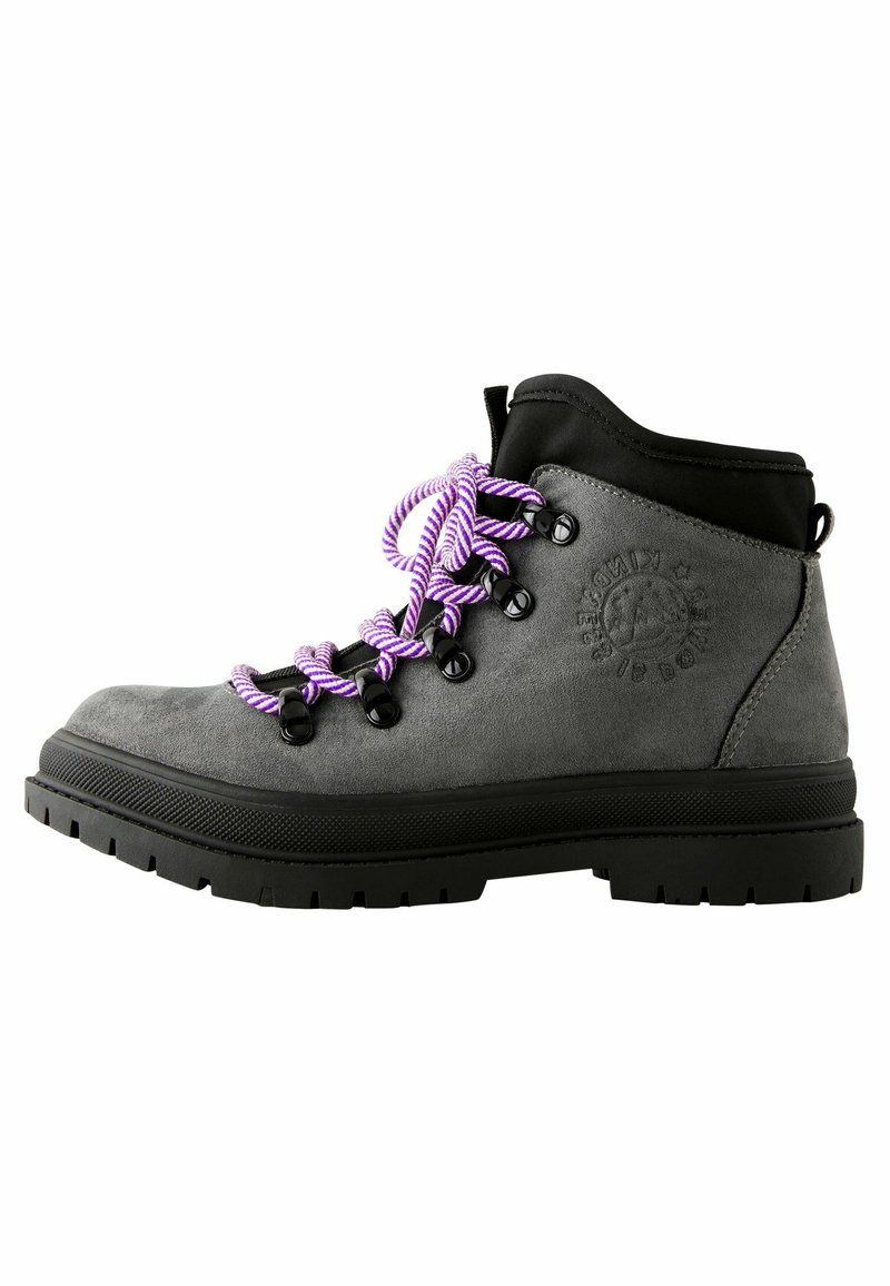 Botte de randonnée en suede gris avec accents noirs, lacets en corde violette, œillets en métal et semelle en caoutchouc noir texturé. Présente un détail de logo embossé.