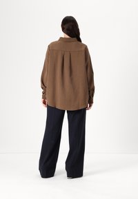 Brown striped oversized shirt with a pleat at the back, paired with navy wide-leg trousers. Long sleeves with buttoned cuffs.