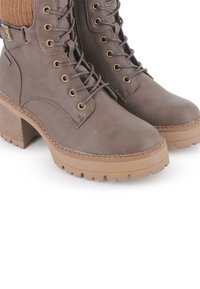 Botas de tobillo marrones con cordones, que presentan un cuello de punto texturizado, una suela de goma duradera y ojales en tono dorado para los cordones.