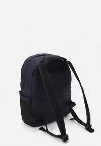 Granatowy plecak wykonany z materiału syntetycznego. Posiada regulowane czarne paski, zapinany na zamek górny oraz boczną siatkową kieszeń na przechowywanie.