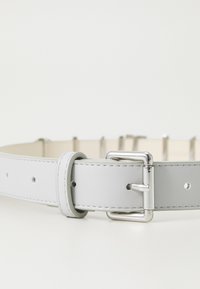 Curea din piele gri cu o cataramă metalică argintie lucioasă, având cusături pe margini și mai multe găuri de ajustare. Design plat.