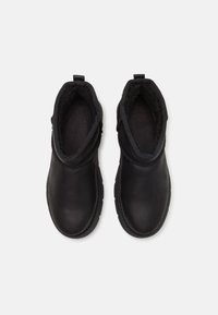 Bottines noires à cheville avec un extérieur en cuir lisse, une doublure intérieure douce et des panneaux élastiques texturés sur les côtés pour un enfilage facile. Semelles en caoutchouc plates.