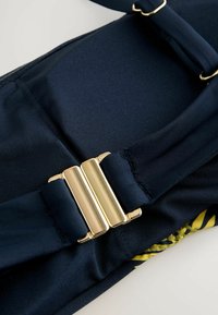 Tamnoplavi kupaći kostim s teksturiranim materijalom i elegantnom zlatnom kopčom. Glatke ivice i živopisni cvjetni uzorak na dnu.