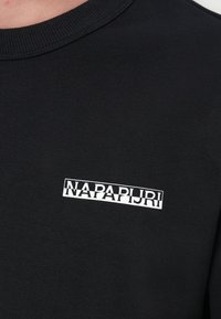 Felpa nera in cotone con scollo a girocollo a coste e patch logo bianco centrato sul petto. Texture liscia.