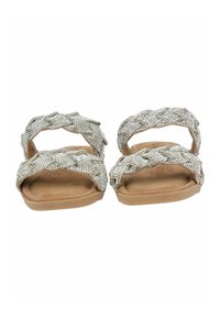 Platte sandalen met een gevlochten ontwerp, voorzien van zilveren versieringen, een zachte beige voetbed en een open teenstijl. Gladde textuur en minimale hardware.