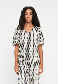 Top à manches courtes en crème avec un motif marine. Design en V, coupe décontractée, en tissu texturé, associé à un pantalon à motif assorti.