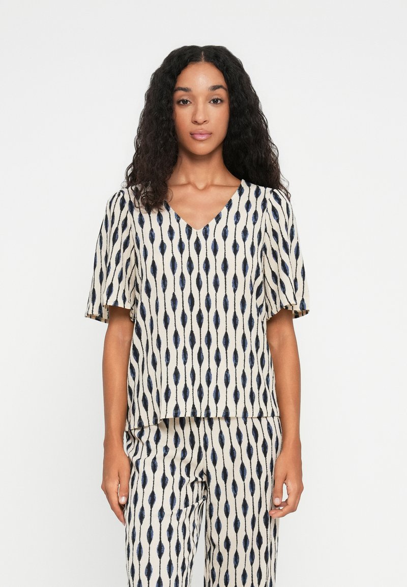 Top à manches courtes en crème avec un motif marine. Design en V, coupe décontractée, en tissu texturé, associé à un pantalon à motif assorti.