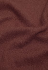 Gros plan sur un tissu doux et texturé de couleur brun rougeâtre foncé, avec un motif de tissage visible et de douces plis créant des ombres et de la profondeur.