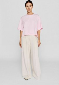 Roze cropped top met korte mouwen, gecombineerd met hoge, wijde crèmekleurige broeken. De outfit heeft een ontspannen, minimalistisch ontwerp.