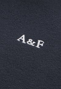 Tejido de punto azul marino oscuro con una textura suave, con las letras blancas bordadas "A & F" exhibidas de manera prominente.