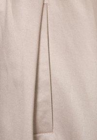 Beżowa tkanina o subtelnej skośnej fakturze, z bocznym zakładanym plisem dla struktury. Gładkie wykończenie z czystymi szwami.