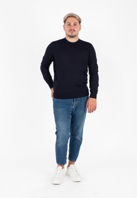 Maglione a coste blu navy, jeans slim-fit azzurri e sneakers bianche. Tessuto liscio, con collo rotondo classico e maniche lunghe.