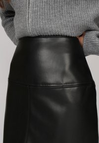 Jupe en cuir noir à taille haute et texture lisse, avec des coutures minimales et un design élégant et ajusté.